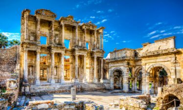 Frontal view of the grand facade of the Celsus Library with its ornate Corinthian columns and intricate sculptures under a bright blue sky.