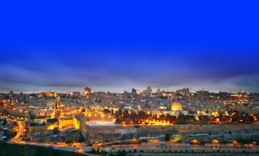 Panoramic view of Jerusalem showcasing the illuminated Dome of the Rock and the city's skyline at dusk, ideal for religious tours.