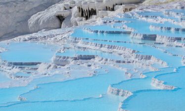 Stunning view of the white travertine terraces of Pamukkale, filled with mineral-rich waters under a clear blue sky.