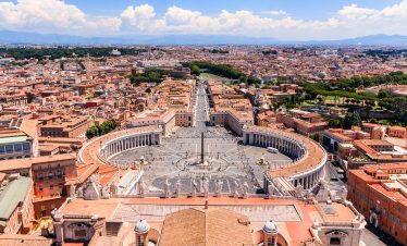Panoramic view of St. Peter's Basilica and the expansive St. Peter's Square in Vatican City, with pilgrims gathering under the majestic dome.