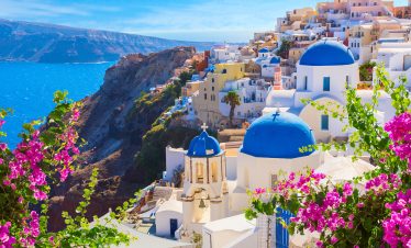 Stunning view of Santorini's white-washed buildings with blue domes overlooking the deep blue Aegean Sea at sunset.