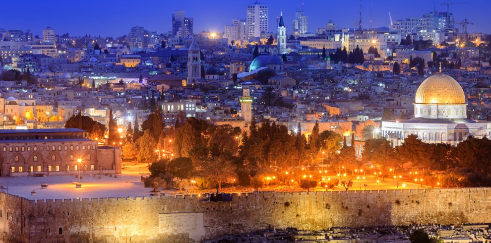 Panoramic view of Jerusalem showcasing the illuminated Dome of the Rock and the city's skyline at dusk, ideal for religious tours.